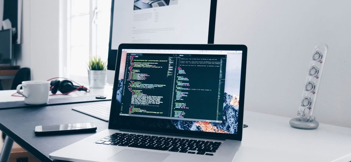 A MacBook with lines of code on its screen on a busy desk