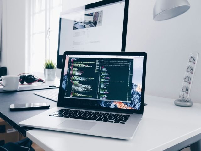 A MacBook with lines of code on its screen on a busy desk